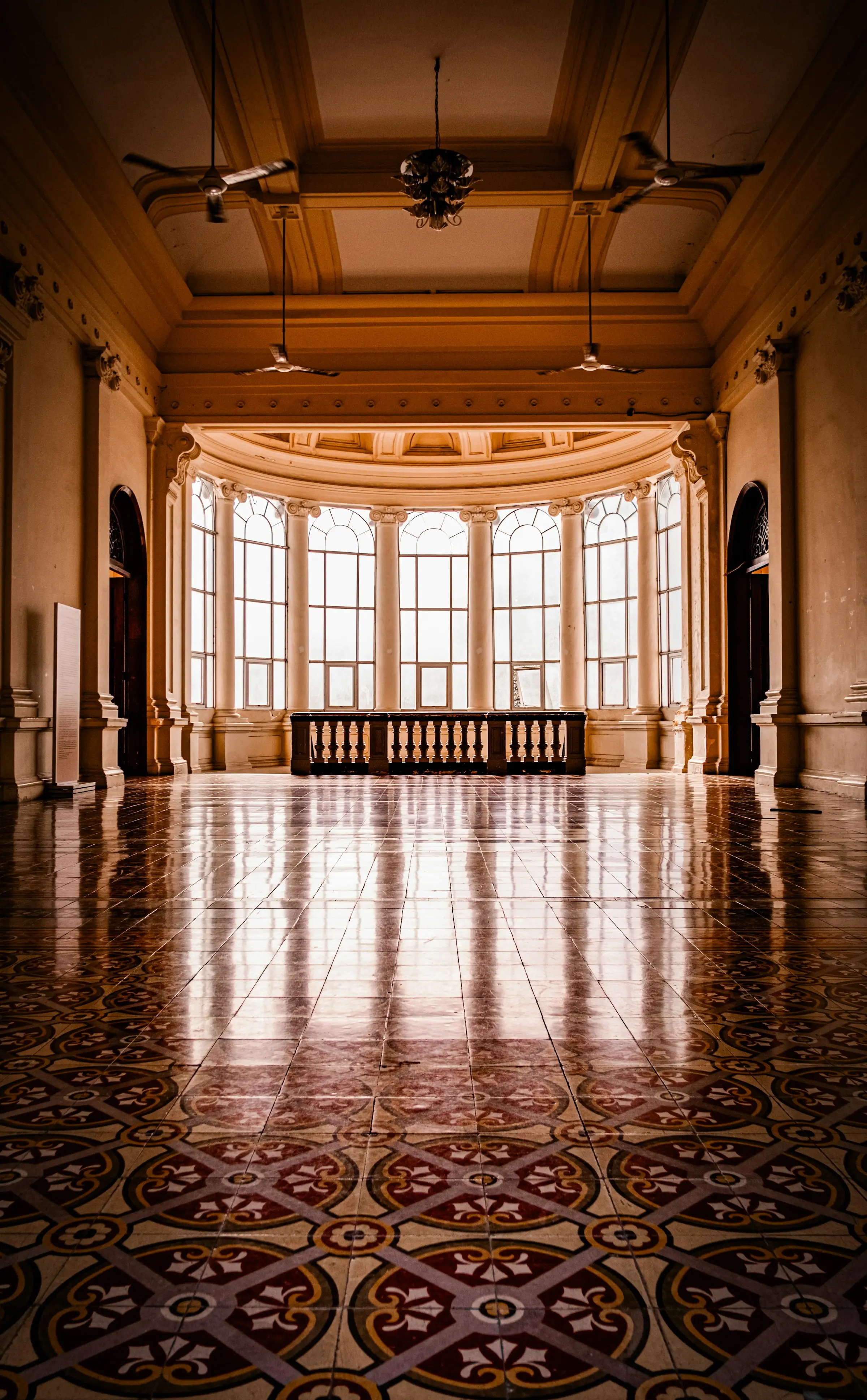 Grand salon vide au sol de carreaux ciment, baie vitrée cintrée laissant entrer la lumière du jour