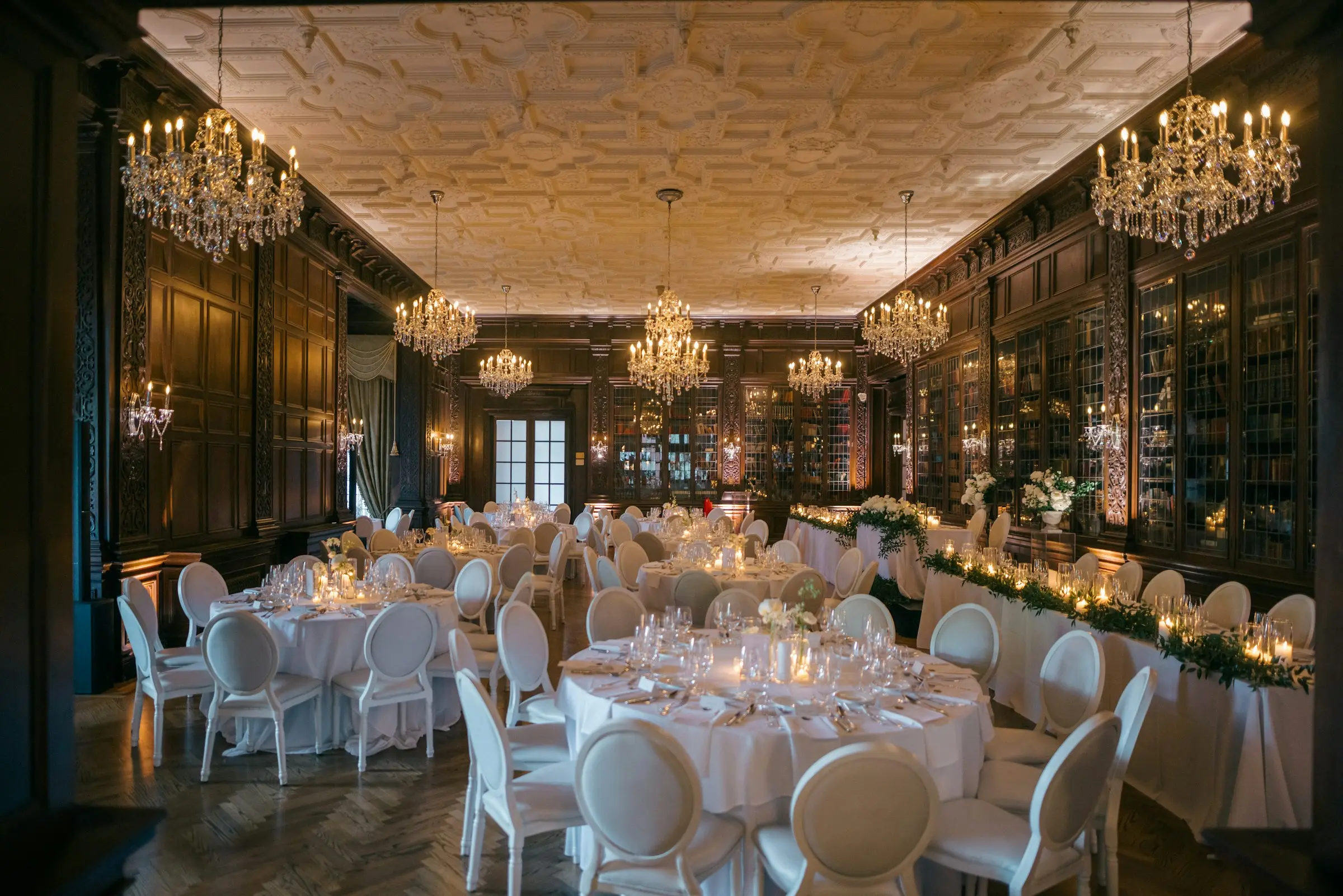 Salle de bal aux boiseries sombres et lustres de cristal, tables rondes nappées de blanc et chaises médaillon