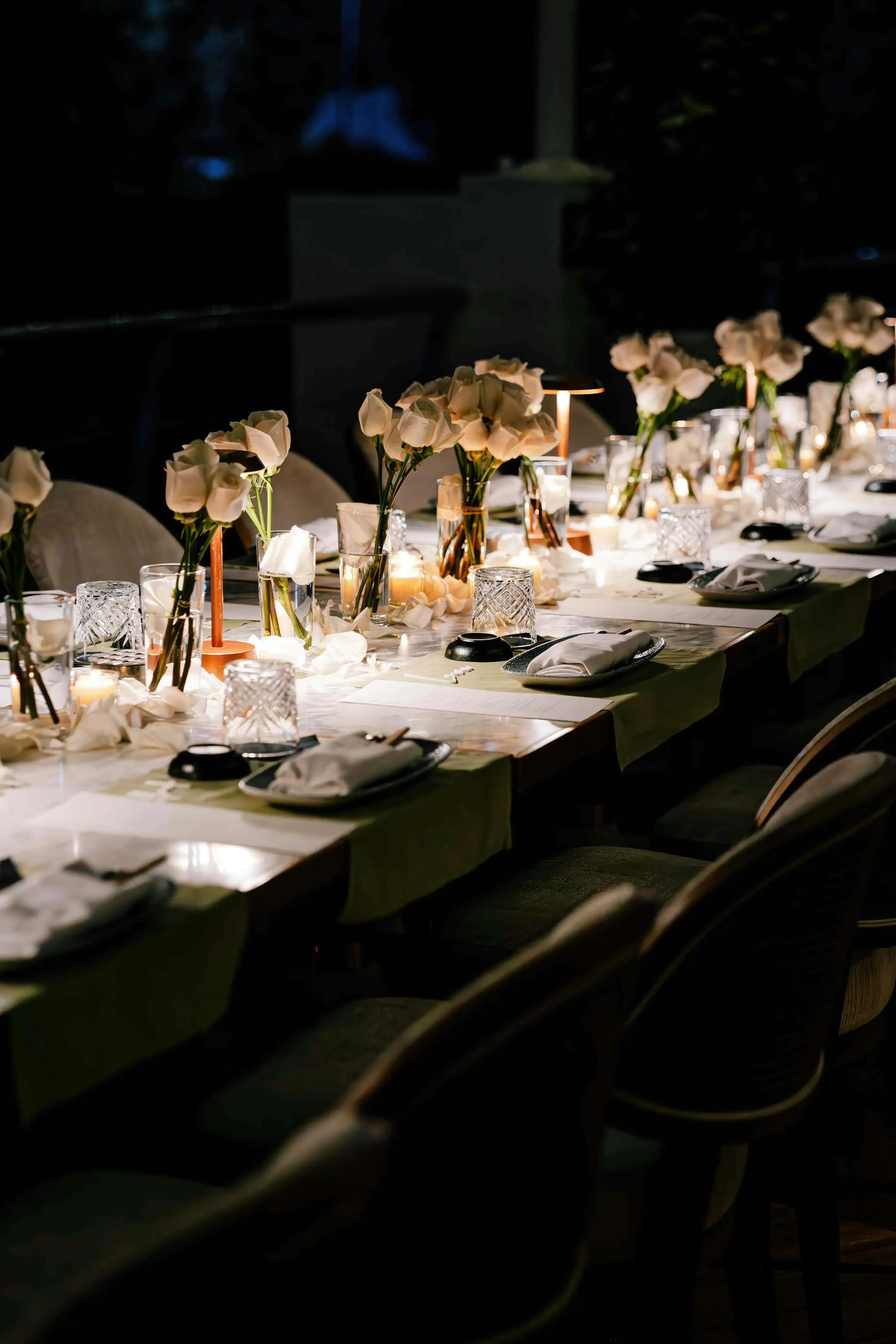 Longue table de réception dressée de nuit, tulipes blanches, bougies et verres en cristal