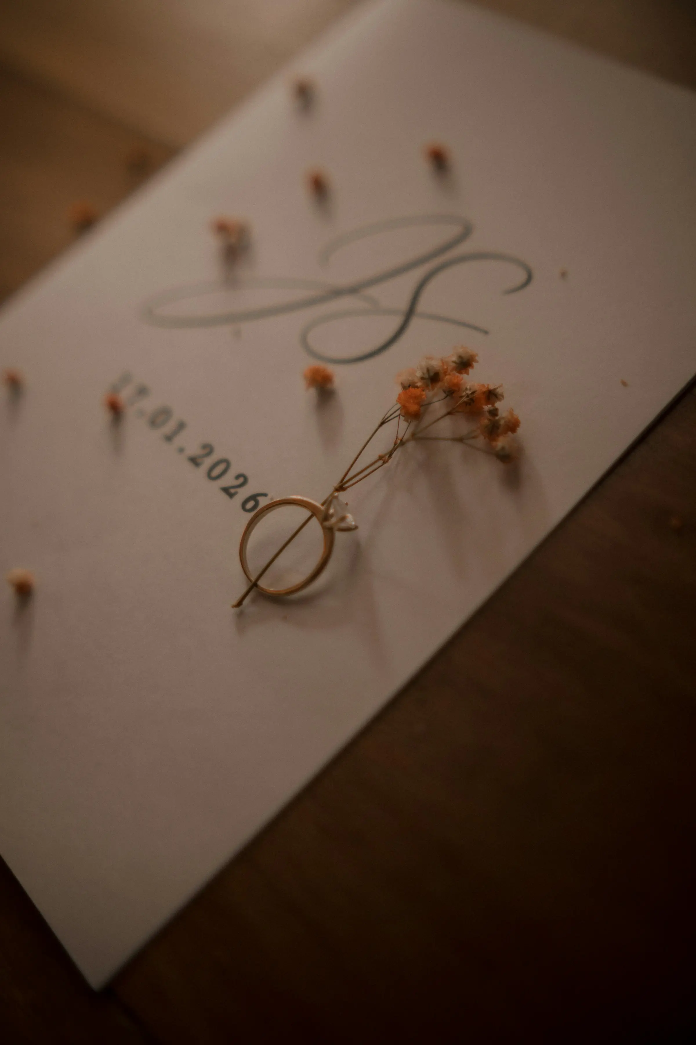 Faire-part de mariage calligraphié, alliance et brins de fleurs séchées sur une table en bois